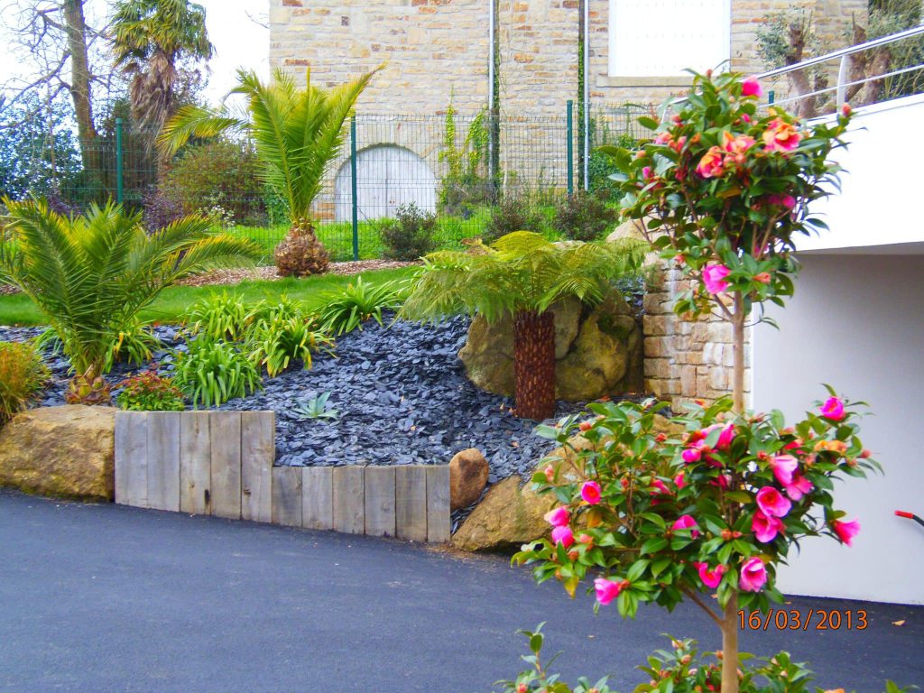 entrée de maison en enrobée avec massif en ardoise roches et poutres paysagères