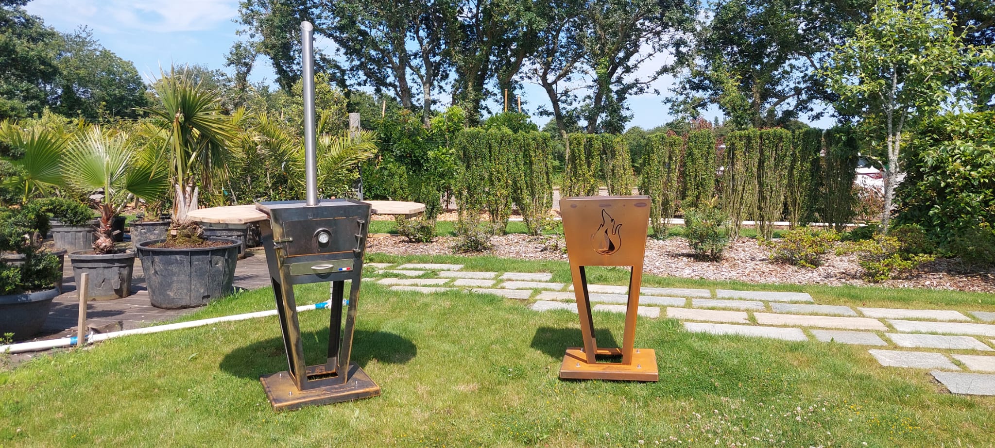 Présentation des braseros TOUSSAINT dans l'espèce showroom de la pépinière, devant des végétaux.